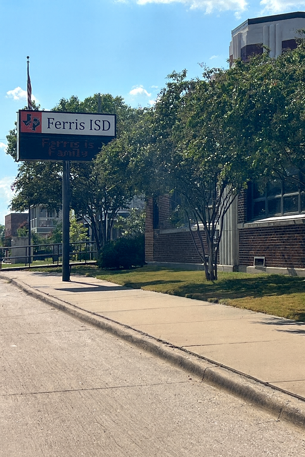 A street view of Ferris ISD sign with the message 'Ferris is Family,' surrounded by trees and a building.
